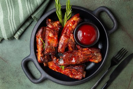 Photo for Black wooden board with baked pork ribs with barbecue sauce, rosemary. Green table background, top view. Meat food. - Royalty Free Image