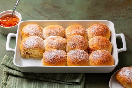 Téléchargez les photos : Rouleaux de pain doux faits maison, petits pains en poudre de sucre et remplis de confiture d'abricot, dans un plateau de cuisson. - en image libre de droit