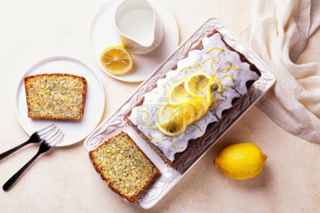 Téléchargez les photos : Vue de dessus du petit déjeuner fait maison. Gâteau tranché avec zeste de citron, sucre et glaçage au citron, graines de pavot sur une assiette blanche et fond clair. - en image libre de droit
