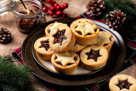 Photo for Traditional british christmas Mince pies on a brown plate, sprinkled with sugar. Also called mincemeat or fruit pie, filled with mincemeat, being a mixture of fruit, spices and suet. Festive Christmas background. - Royalty Free Image