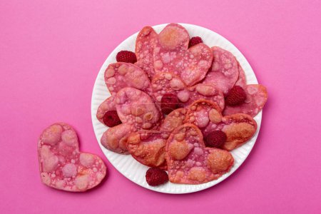 Photo for Heart shaped pink sweet cookies, fried angel wings, coloured with beetroot. Valentine day romantic breakfast with raspberries, white background, top view. Bright pink background. - Royalty Free Image