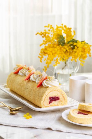 Photo for Women's Day breakfast on March 8. Rolled sponge Mimosa cake filled with custard cream and berry jelly, strawberries.. Morning table, coffee cups, flower bouquet. Vertical image. - Royalty Free Image