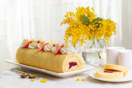 Photo for Women's Day breakfast on March 8. Rolled sponge Mimosa cake filled with custard cream and berry jelly, strawberries.. Morning table, coffee cups, flower bouquet. Light holiday background. - Royalty Free Image