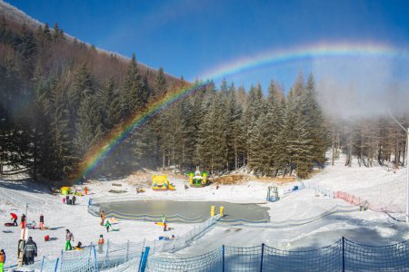 Photo for Family winter ski resort Il Lago della Ninfa. Monte Cimone, mountains in the northern Apennines, of Italy, Emilia-Romagna. Slope for children sleighing, snow tubing. Rainbow. People figures, silhouettes. - Royalty Free Image