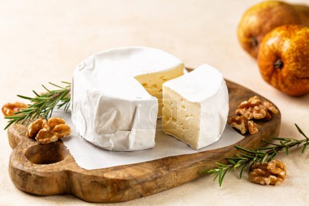 Foto de Caciotta, queso italiano cremoso y suave. Un queso para principiantes sobre una tabla de madera, con nueces, peras y romero. - Imagen libre de derechos