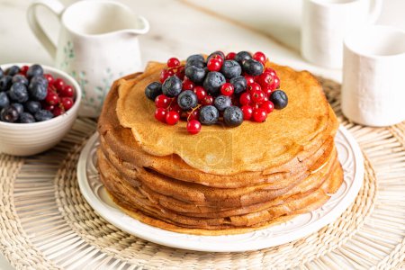 Stack of sweet homemade crepes, type of thin pancake, with blueberry and red currant. Breakfast on a white table.