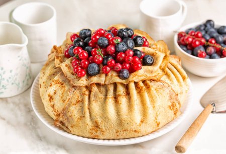 Homemade crepe cake, made of type of thin pancake and cream, decorated with blueberry and red currant, served on a white table