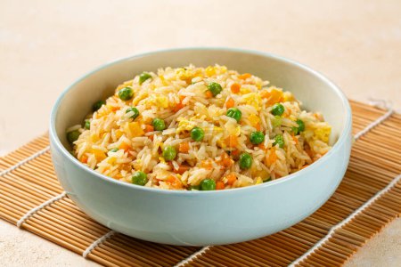 Foto de Tazón con arroz frito con huevo y verduras, cebolla, pimiento, zanahoria, guisantes verdes. Preparado y servido en un plato azul claro. - Imagen libre de derechos