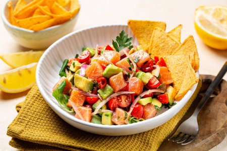 Photo for Close up of salmon ceviche, a fish dish, salmon marinated in citrus and seasonings, avocado, tomato and red onion, parsley. Corn chips nachos. Peruvian,  Mexican, Spanish-American countries dish. - Royalty Free Image