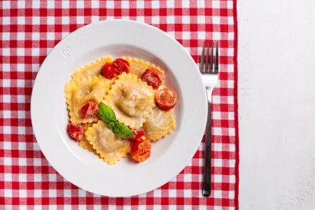 Téléchargez les photos : Vue du dessus d'une assiette avec des raviolis italiens crémeux aux tomates et au fromage. Table avec nappe d'échecs rouge et blanche traditionnelle. Espace de copie. - en image libre de droit