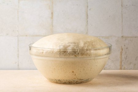 Photo for Glass bowl with fresh homemade yeast dough on a kitchen table. - Royalty Free Image