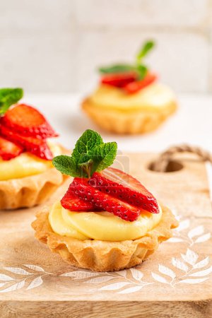 Photo for Strawberry tartlets with vanilla pastry cream - mini fruit tarts filled with custard vanilla pastry cream in a cookie crust. Homemade Dessert on awooden board, Vertical image. - Royalty Free Image