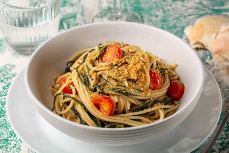 Italienische Pasta. Spaghetti mit agretti oder salsola soda, Tomaten, Semmelbrösel, Pinoli-Pinienkernen in einem weißen Teller.