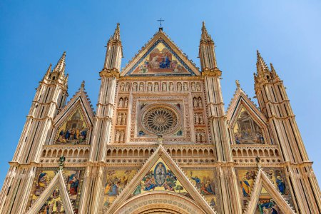 Foto de La fachada de la Catedral de Orvieto, Duomo di Orvieto, Umbría, Italia. Frontera dorada, decorada con grandes bajorrelieves y estatuas con los símbolos de los evangelistas. - Imagen libre de derechos