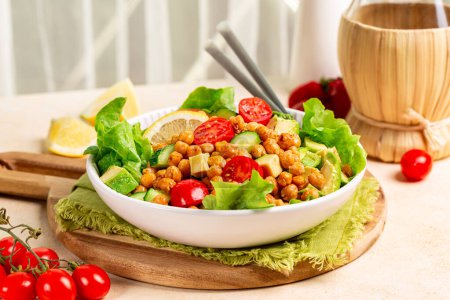 Photo for Kitchen table with mediterranean chickpea salad. Chickpea and paprika baked beans, lettuce, tomatoes, avocado, cucumber, lemon and olive oil dressing. Healthy high protein vegan meal. - Royalty Free Image