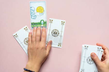 Téléchargez les photos : Mains de Fortune femme caissière et cartes de tarot blanc. Pile de carte classique de Rider Waite pont sur fond rose - en image libre de droit