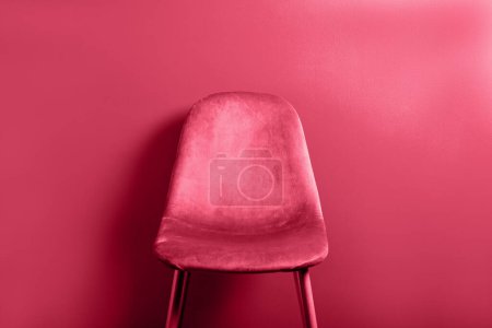 Foto de Moderna silla de terciopelo rosa en patas de madera, imagen tonificada en viva magenta, color del año 2023 - Imagen libre de derechos