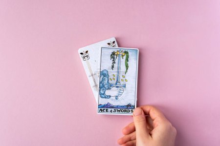 Foto de London, UK: 6 January, 2023: Minor Arcana - Ace of Swords of Tarot Card of Rider Waite deck in hand on pink background - Imagen libre de derechos