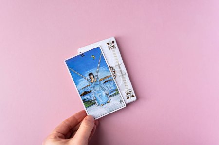 Foto de London, UK: 6 January, 2023: Minor Arcana - Two of Swords of Tarot Card of Rider Waite deck in hand on pink background - Imagen libre de derechos
