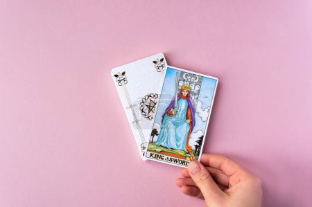 Foto de London, UK: 6 January, 2023: Minor Arcana - King of Swords of Tarot Card of Rider Waite deck in hand on pink background - Imagen libre de derechos