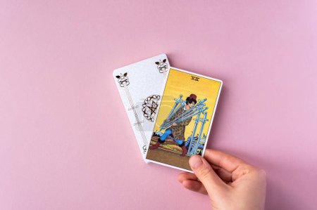 Foto de London, UK: 6 January, 2023: Minor Arcana - Seven of Swords of Tarot Card of Rider Waite deck in hand on pink background - Imagen libre de derechos