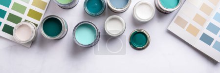 Tiny sample paint cans during house renovation, process of choosing paint for the walls, different blue, green and white colors, color charts on background, banner size