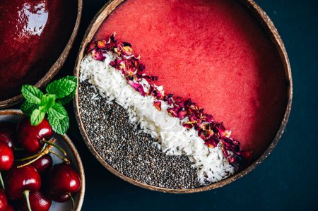 Photo for Pink Smoothie from Banana and Strawberries with pieces of Strawberries, Coconut Shreds, Chia Seeds and rose petals on top in the Coconut Shell Bowl - Royalty Free Image