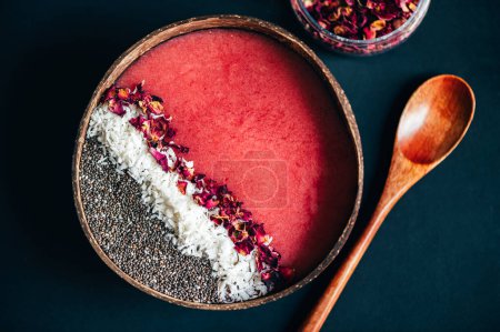 Photo for Pink Smoothie from Banana and Strawberries with pieces of Strawberries, Coconut Shreds, Chia Seeds and rose petals on top in the Coconut Shell Bowl - Royalty Free Image