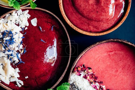 Photo for Variety of different smoothies: Banana and Strawberries, Cherry and Apple with pieces of Strawberries, Coconut Shreds, Chia Seeds and rose petals on top in the Coconut Shell Bowl - Royalty Free Image