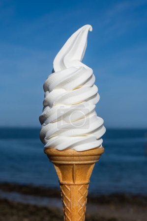 Soft whipped vanilla ice cream with chocolate stick in waffle cone in hands on blue sky background