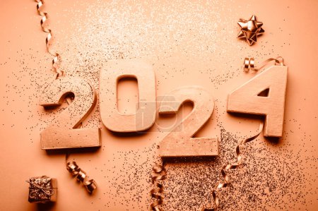 Golden digits 2024 with glitter and xmas decorations nearby. Holiday Party Decoration or postcard concept with top view and copy space. Toned in Peach Fuzz color of the year 2024