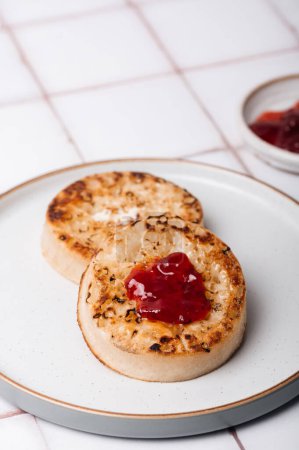Hot Toasted Crumpets with piece of butter on a plate with strawberry jam. Perfect tasty breakfast popular in England, UK