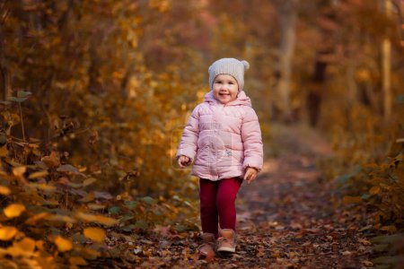 Téléchargez les photos : Portrait of beautiful happy child walking on autumn colorful leaves and grass background. Funny girl outdoors in fall park. - en image libre de droit