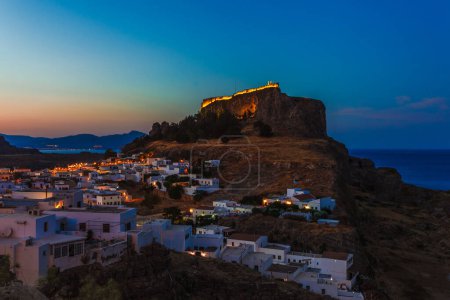 Photo for Scenic landscape photo of night Lindos town and castle on Rhodes island, Dodecanese, Greece. Panorama with bright lights, mountains and sea. Famous tourist destination in South Europe - Royalty Free Image