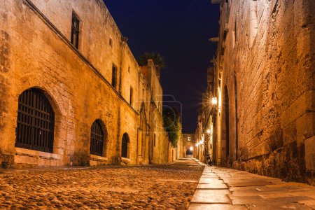 Téléchargez les photos : Photo de nuit de l'ancienne rue des Chevaliers dans la ville de Rhodes sur l'île de Rhodes, Dodécanèse, Grèce. Murs en pierre et veilleuses lumineuses. Destination touristique célèbre en Europe du Sud - en image libre de droit
