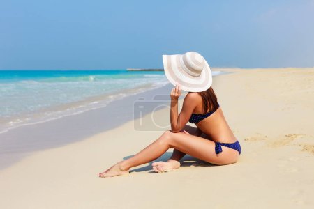 Foto de Atractiva espalda de hermosa mujer irreconocible relajante y tomando el sol en bikini sobre fondo de mar y palma. Nalgas sexys. Playa en Dubai, Emiratos Árabes Unidos famoso destino turístico - Imagen libre de derechos