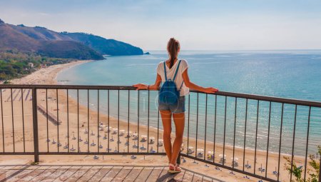Photo for Young tourist woman on the beach and sea landscape with Sperlonga, Lazio, Italy. Scenic resort town village with nice sand beach and clear blue water. Famous tourist destination in Riviera de Ulisse - Royalty Free Image