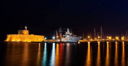 Téléchargez les photos : Photo de nuit de l'ancienne forteresse et jetée dans la ville de Rhodes sur l'île de Rhodes, Dodécanèse, Grèce. Murs en pierre et veilleuses lumineuses. Destination touristique célèbre en Europe du Sud - en image libre de droit