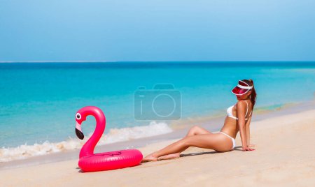 Téléchargez les photos : Tourisme belle femme de vacances en bikini et chapeau à Dubaï. Modèle de plage prêt à se détendre avec flamant rose drôle. Voyage femme dans la célèbre destination EAU. Élégante dame bronzer profiter des vacances de voyage - en image libre de droit