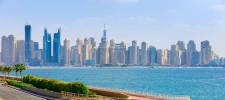 Téléchargez les photos : Vue panoramique du centre-ville de Dubaï avec palmiers et gratte-ciel. Journée d'été ensoleillée sur la côte de Dubaï. Dubaï est la destination touristique la plus célèbre des EAU. Endroit idéal pour voyager et se reposer de luxe - en image libre de droit