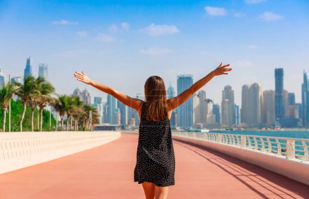 Foto de Mujer turística disfrutando de la vista de Dubai con palmeras y rascacielos. Día soleado de verano en el desierto de Dubai. Dubai es un famoso destino turístico en los Emiratos Árabes Unidos. Lugar ideal para viajes de lujo y descanso - Imagen libre de derechos