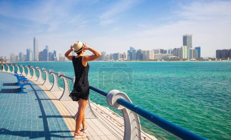 Photo for Tourist woman enjoying view of Abu Dhabi with sea and skyscrapers. Sunny summer day in Abu Dhabi - famous tourist destination in UAE. Ideal place for luxury travel and rest - Royalty Free Image
