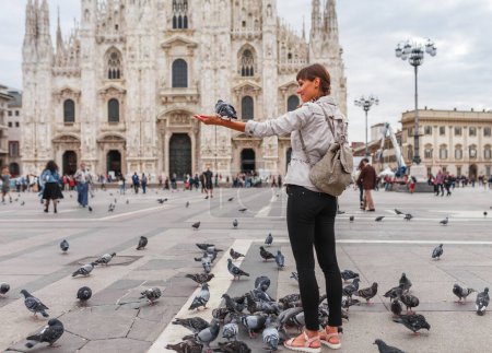Téléchargez les photos : Voyage touriste femme nourrit colombes près de Duomo di Milano - l'église cathédrale de Milan en Italie. Fille profiter sur la place dans le centre-ville, destination célèbre pour le voyageur - en image libre de droit