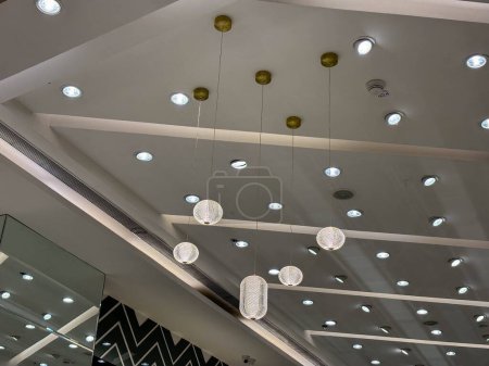 Esta imagen muestra una amplia habitación llena de numerosas luces modernas que cuelgan del techo, iluminando la zona con un brillo brillante e incluso. Las luces varían en tamaño y forma, creando una interesante pantalla visual.