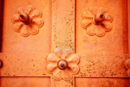 Großaufnahme eines Bildes, das die Textur und Symmetrie orangefarbener floraler Metallmuster an einer Tür zeigt und komplizierte Kunstfertigkeit und Design hervorhebt.