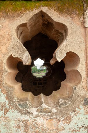 Eine detaillierte Ansicht eines aufwändig geschnitzten antiken Steinfensters in einer alten, verwitterten Wand, durch die natürliches Licht einfällt, das die historische Architektur im Ahaz Mahal, Mandu, Indien widerspiegelt.
