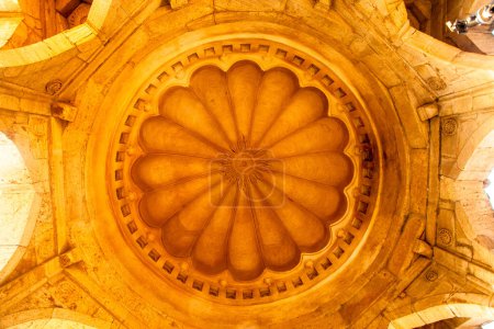 An upward view of a stunning, ornate dome ceiling with intricate patterns and warm lighting radiating a sublime atmosphere at Mandu, India