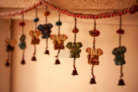 Una fila de campanas cuelgan del techo, cada una con una cabeza de elefante de diferentes colores. Las campanas cuelgan en una línea, con algunos colgando más alto que otros. Los elefantes son todos de diferentes tamaños