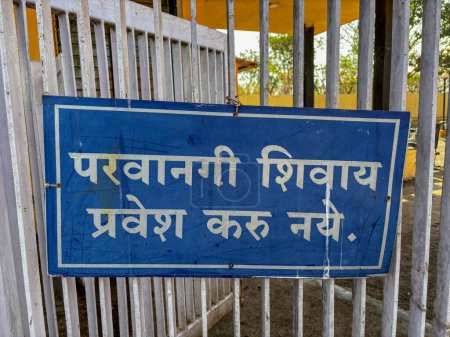 Un letrero azul con el idioma marathi extranjero escrito en él cuelga en una cerca que dice 'deje el pie afuera'. Se muestra fuera del templo.