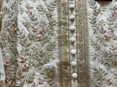 A white dress with flowers embroidered on it. The flowers are in different colors and sizes. The dress has a button on the side
